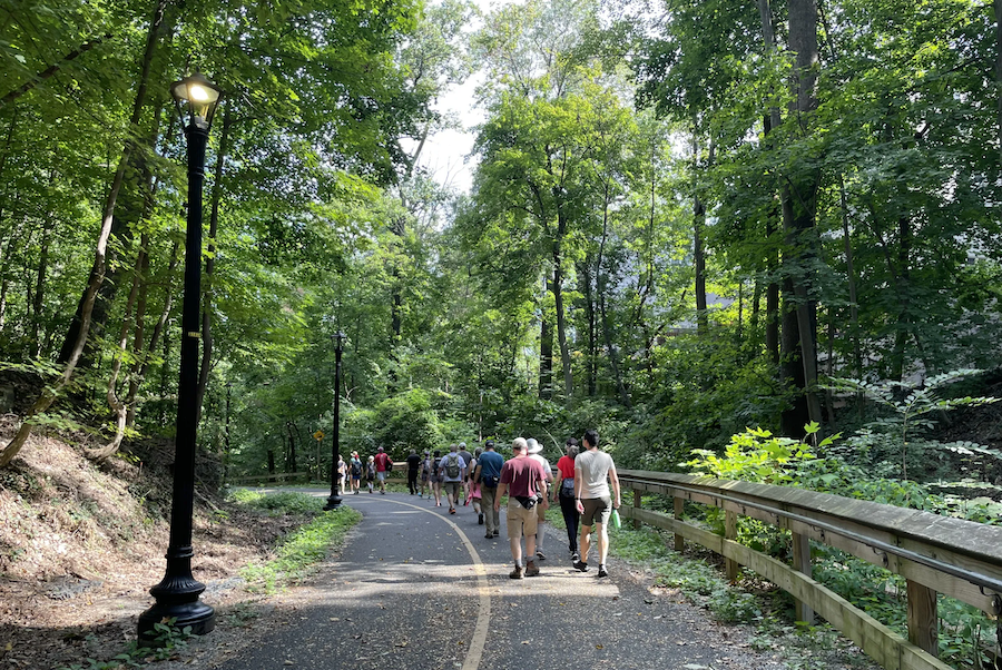 A group of hikers walk along a shaded trail in Rock Creek Park on a sunny day.